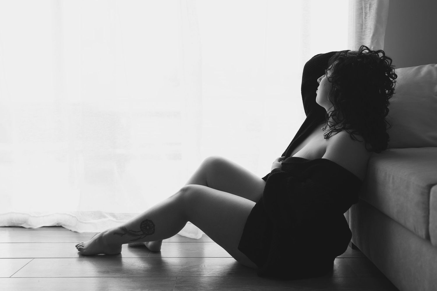 Black and white artistic boudoir photograph showing a person in lace lingerie from behind with long wavy hair.