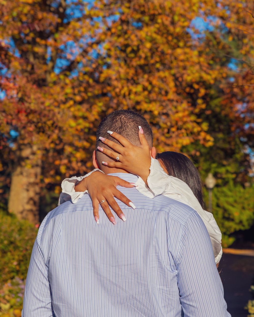 Couple embracing outdoors with autumn foliage in background showing hands wrapped around in a loving gesture.