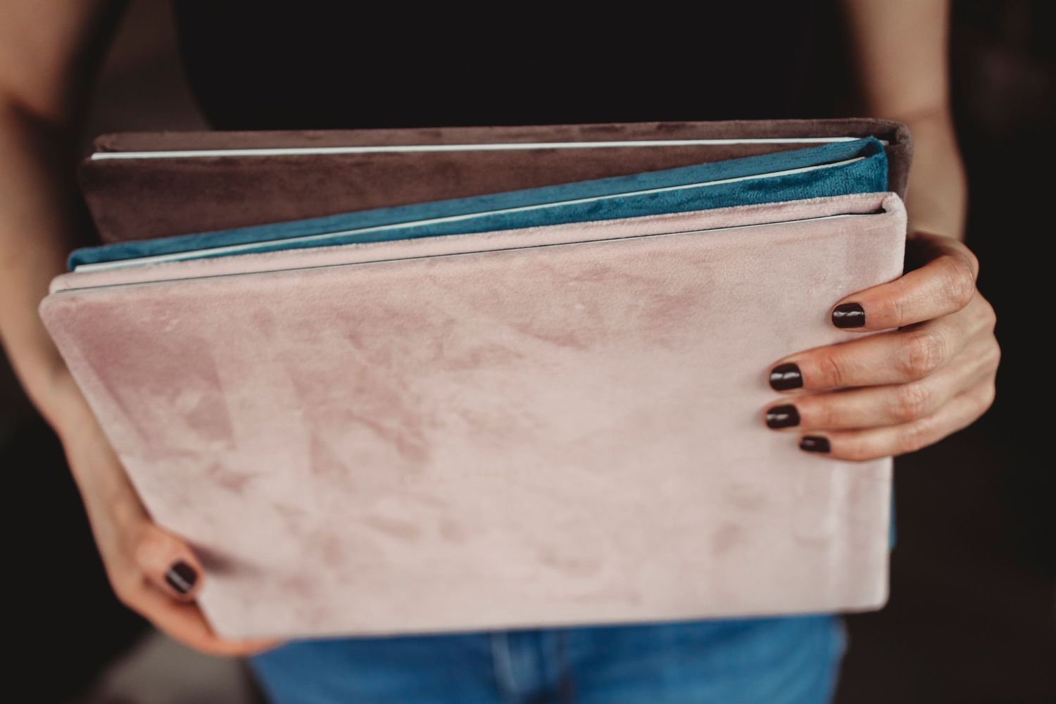 Close-up view of hands with black nail polish holding pink and blue folders.