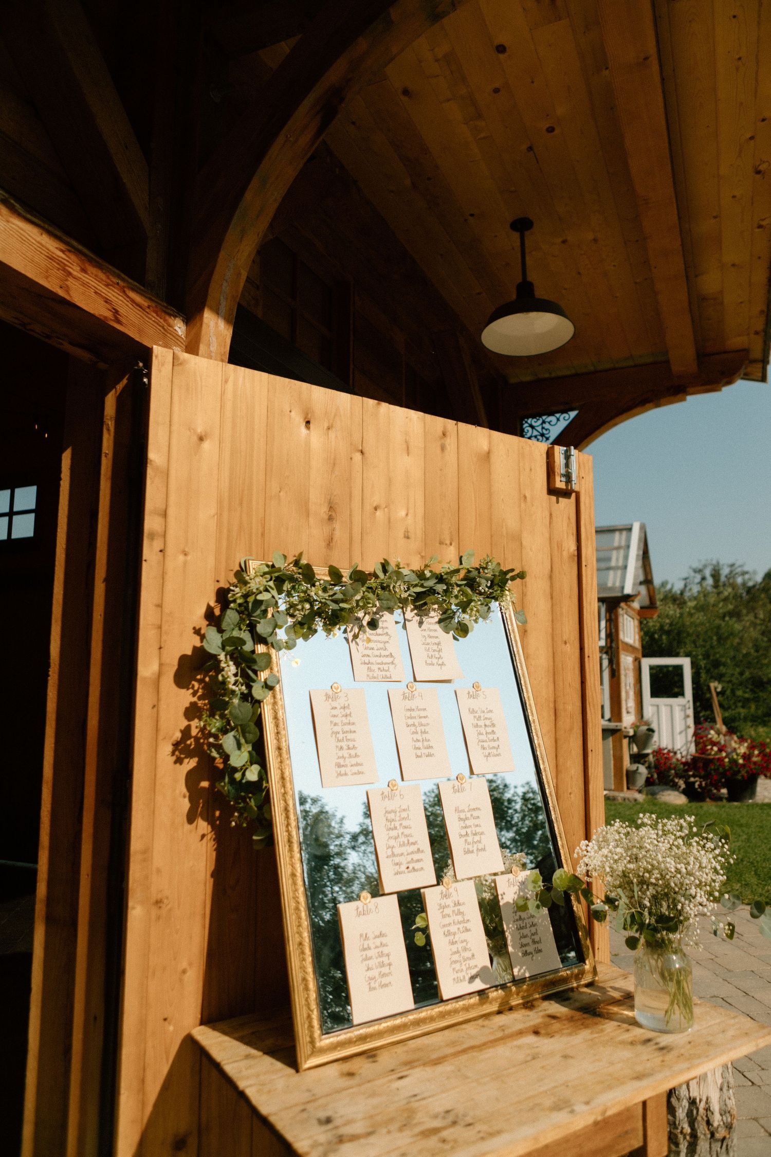 Rustic wooden seating chart with greenery garland displayed at outdoor wedding venue.