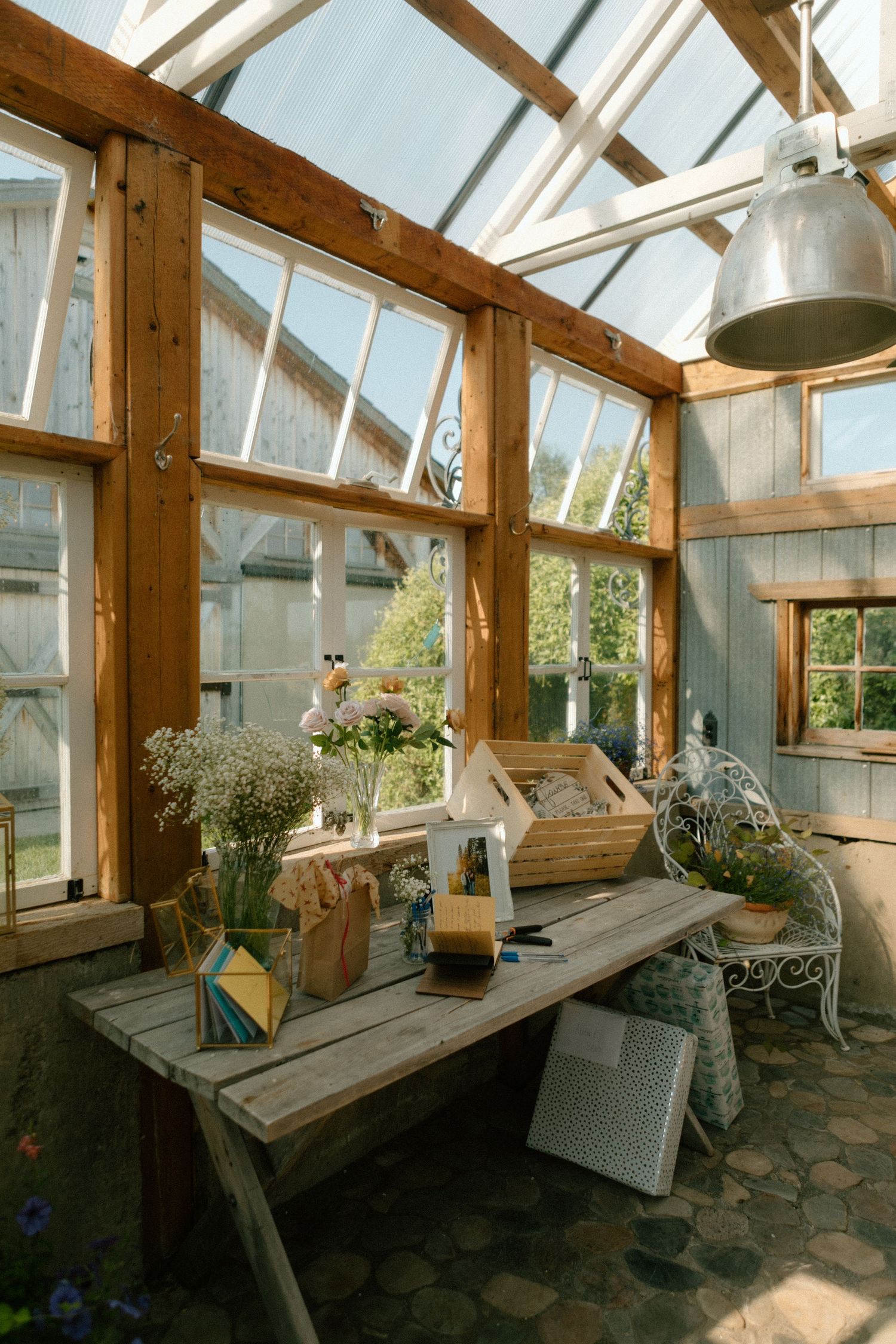 Sunlit greenhouse interior with wooden beams, rustic furniture and potted flowers on a weathered table.