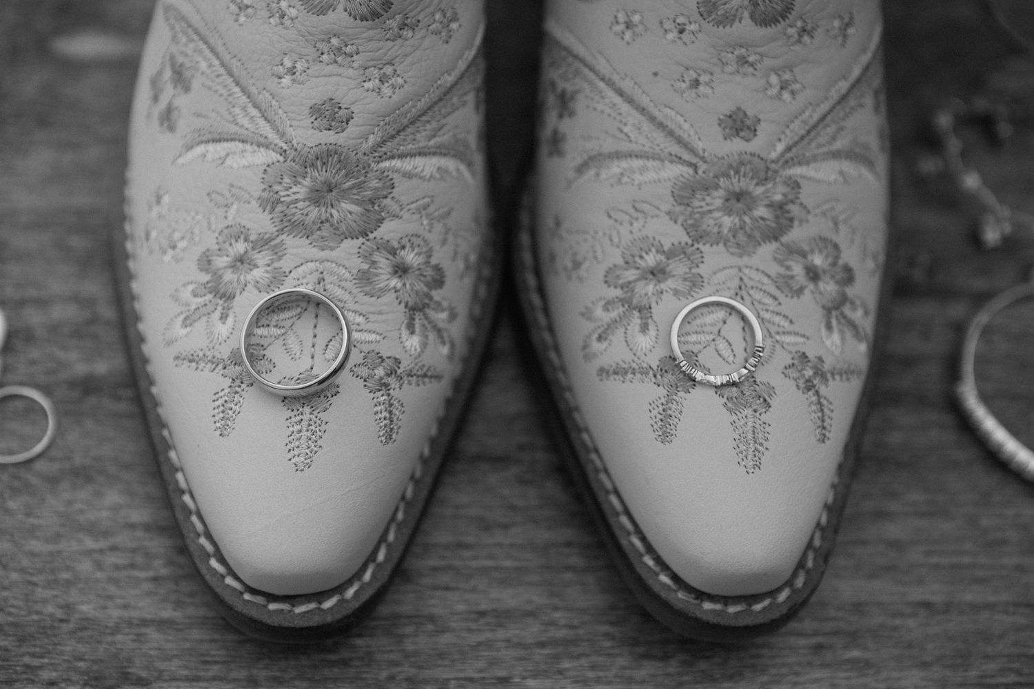 Wedding rings rest on top of embroidered white cowboy boots in black and white photography.