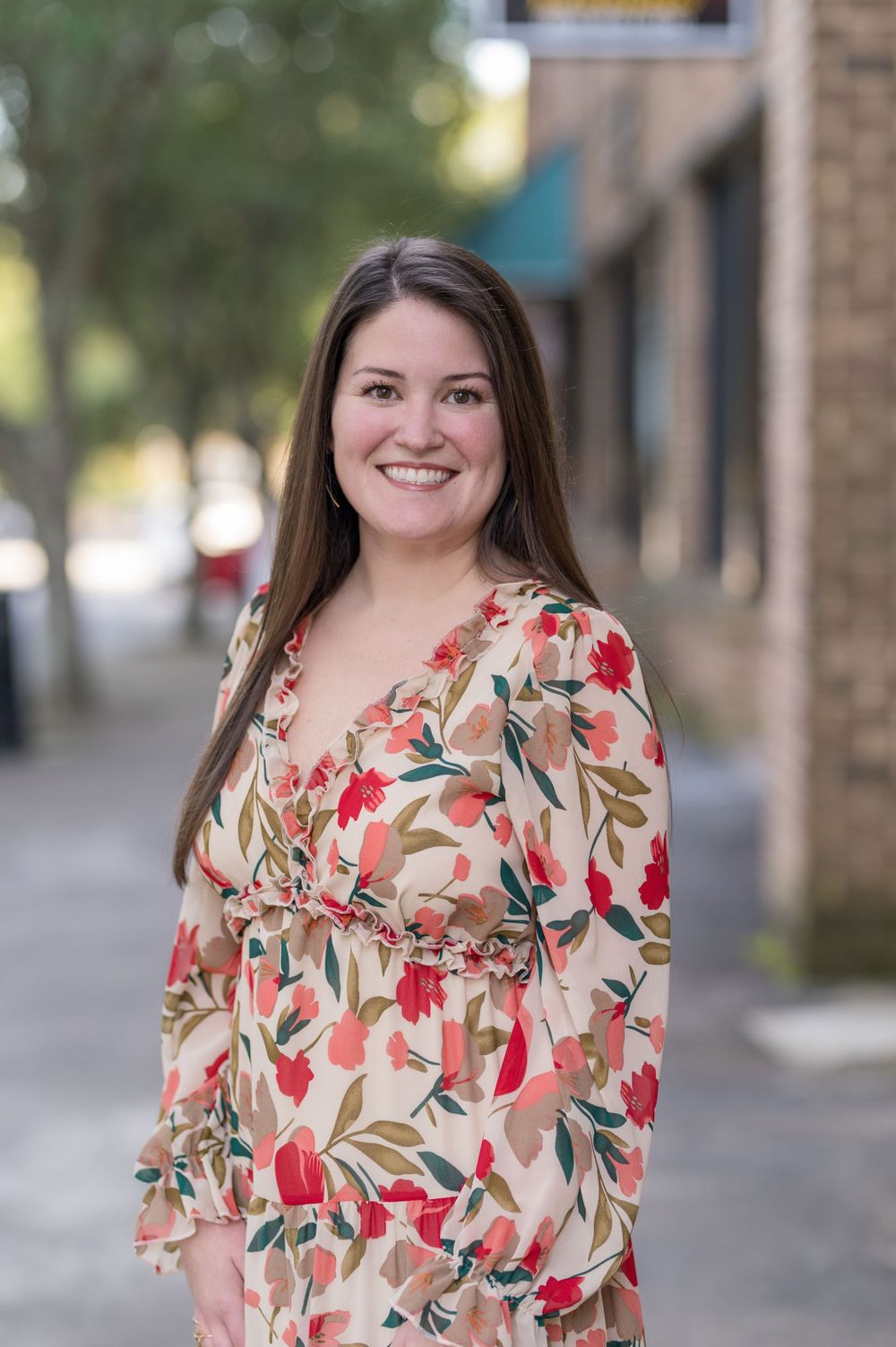Outdoor portrait of person wearing beige and red floral dress in urban setting.