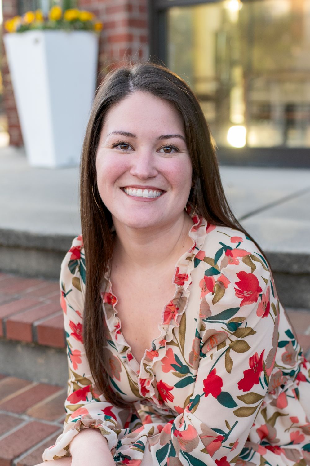 Portrait of person in floral print dress reclining against brick wall with warm lighting.
