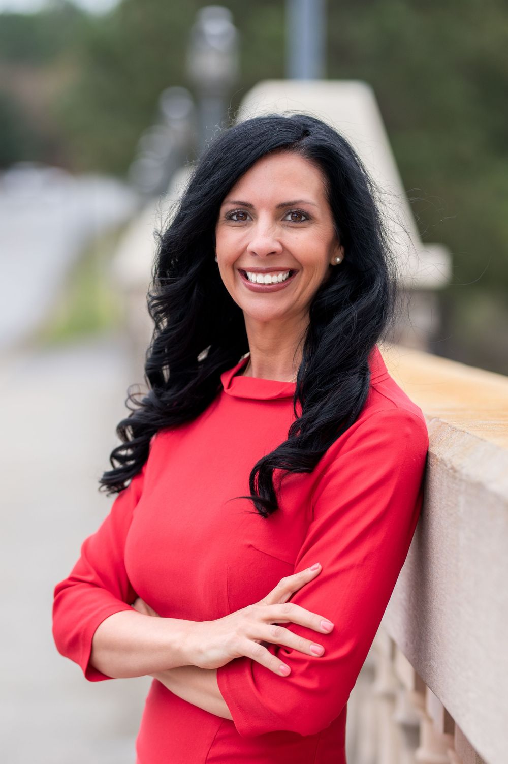 Professional in bright red turtleneck poses with crossed arms against outdoor backdrop.