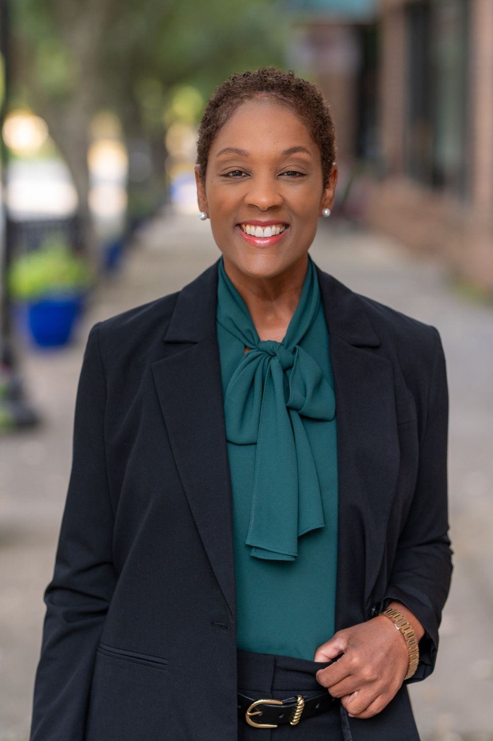 Professional portrait of person in navy blazer and green tie-neck blouse standing outdoors.