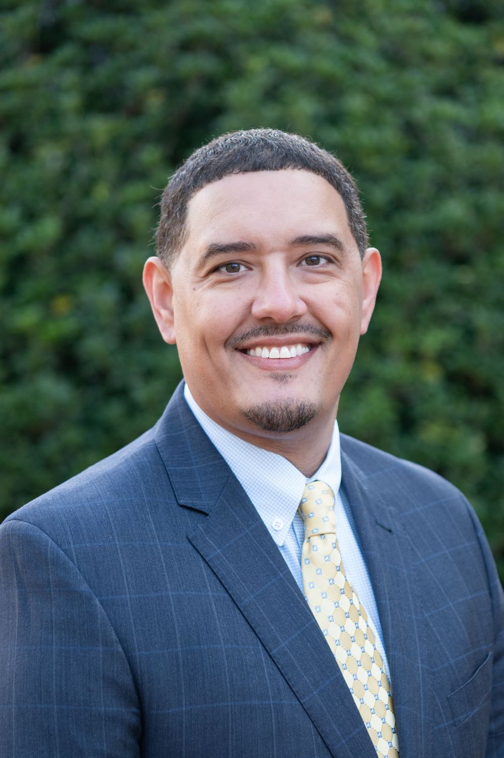 Business portrait of person in navy suit with yellow patterned tie against green background.