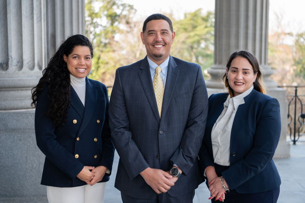 Professional group photo of three people in business attire standing between classical columns.