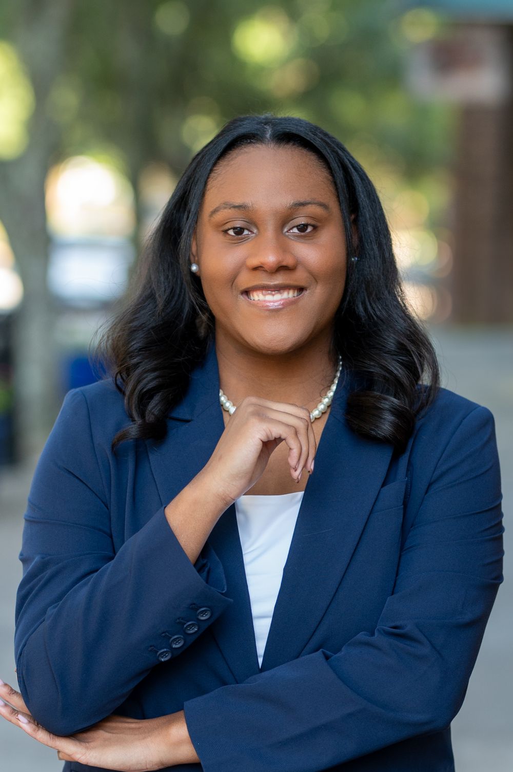 Business headshots of person in navy blazer and white top against urban background.