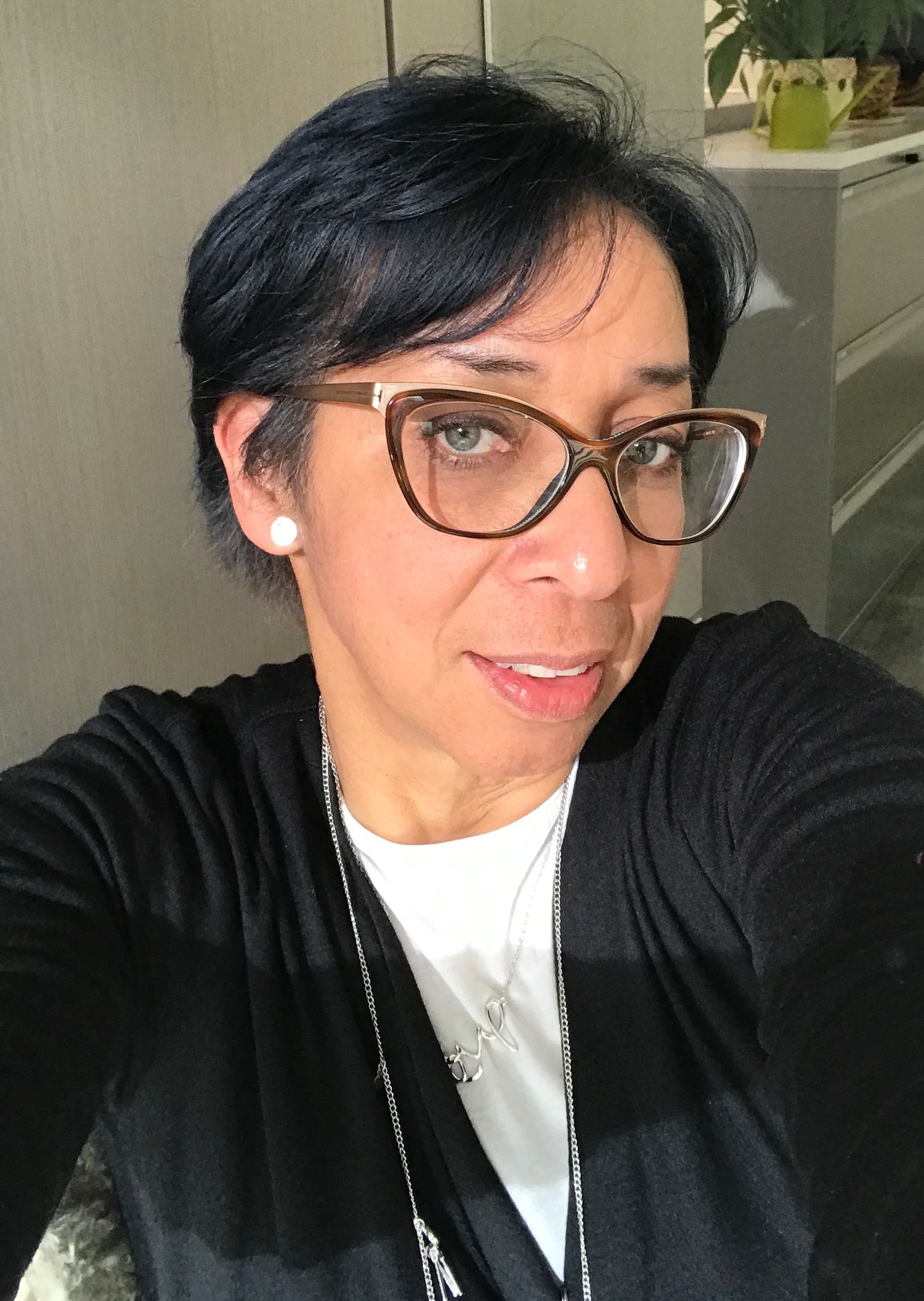 Person in black cardigan and white shirt taking a selfie with glasses and short dark hair.