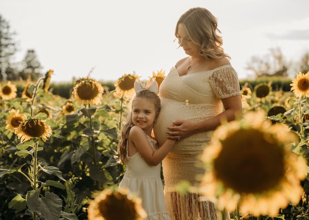 A tender maternity portrait amidst blooming sunflowers during golden hour.