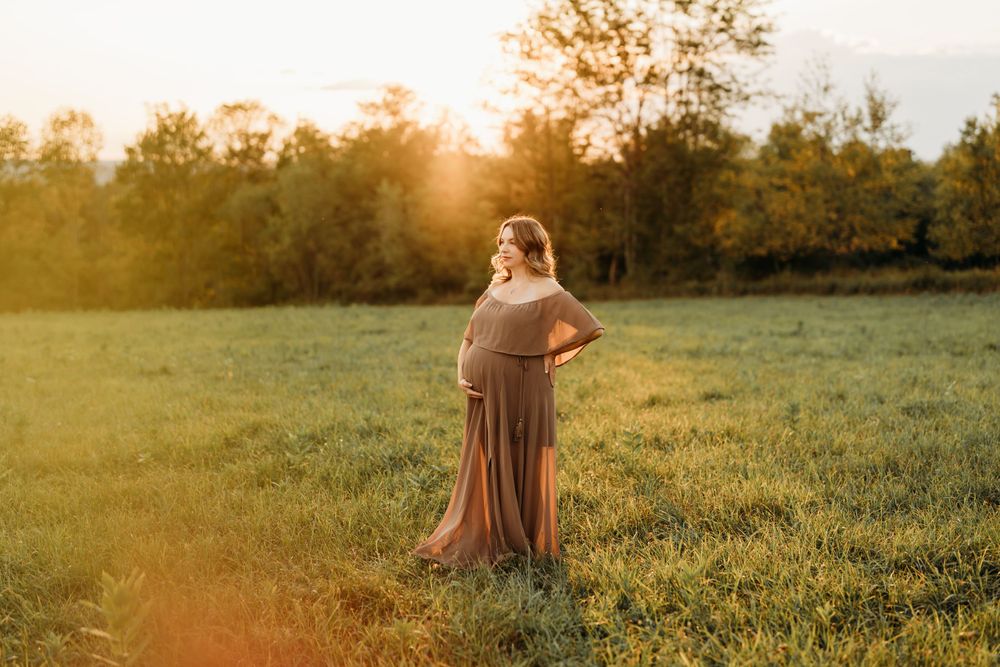 A person in a brown dress stands in a sun-lit meadow during golden hour.
