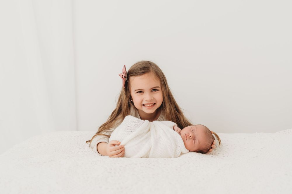 Two siblings laying together on white backdrop during professional photo session.