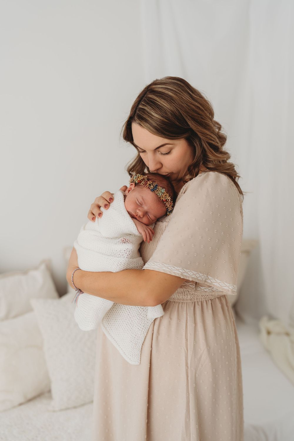 Tender moment between parent and swaddled newborn in soft natural light studio setting.