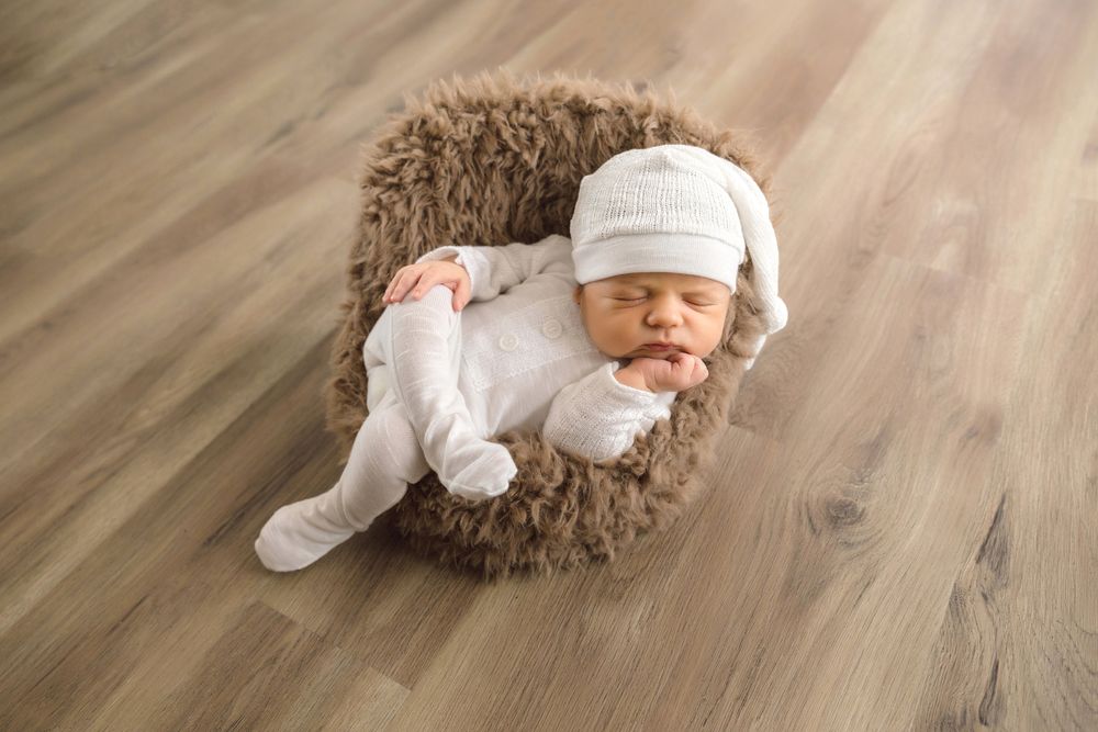 Baby wearing white clothing crawling on wooden floor with natural lighting.