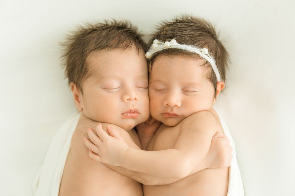 Two newborn twins sleeping peacefully while embracing each other, wrapped in white cloth.