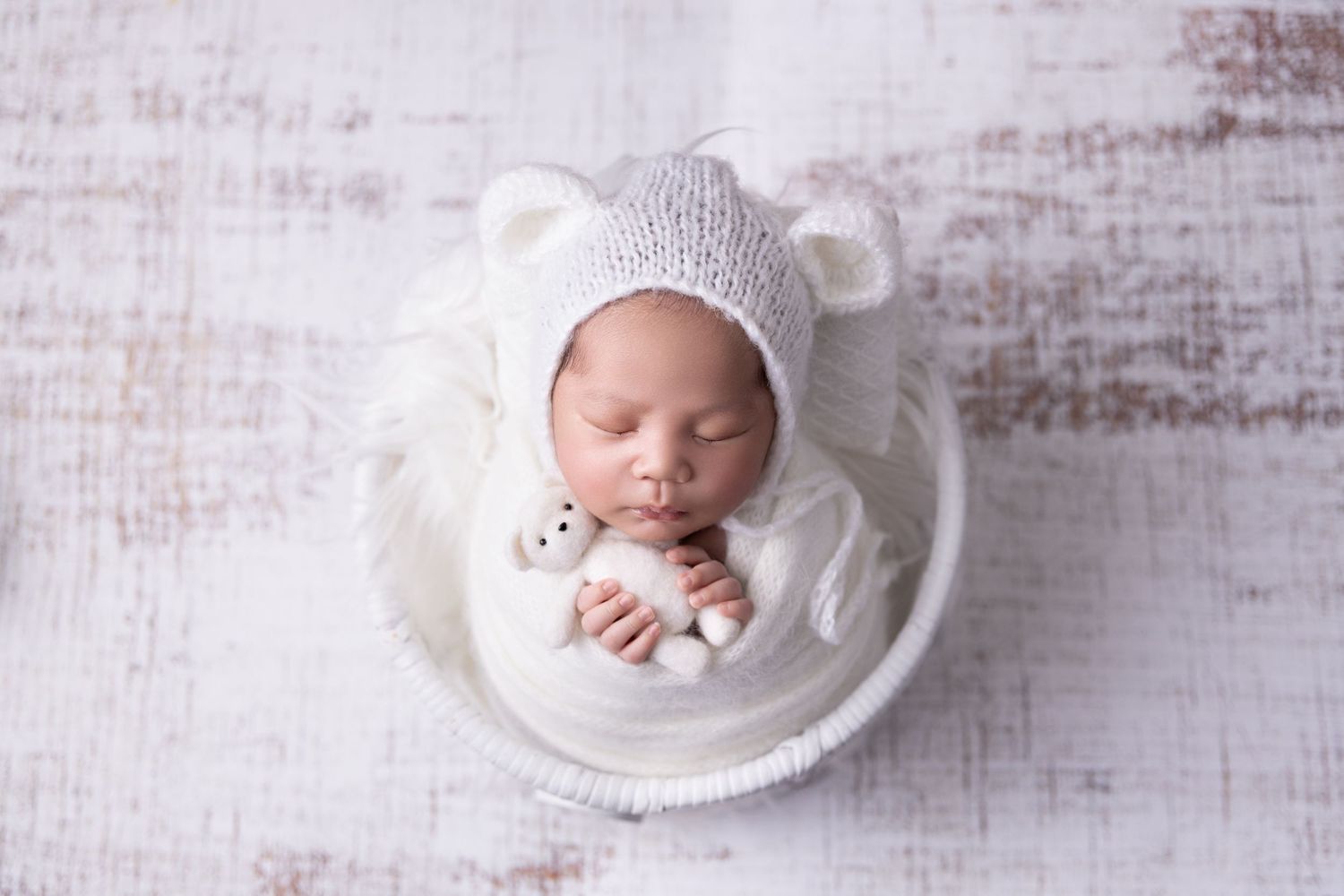 A sleeping newborn swaddled in pink fabric lies on fluffy pink fur surrounded by matching pink roses.