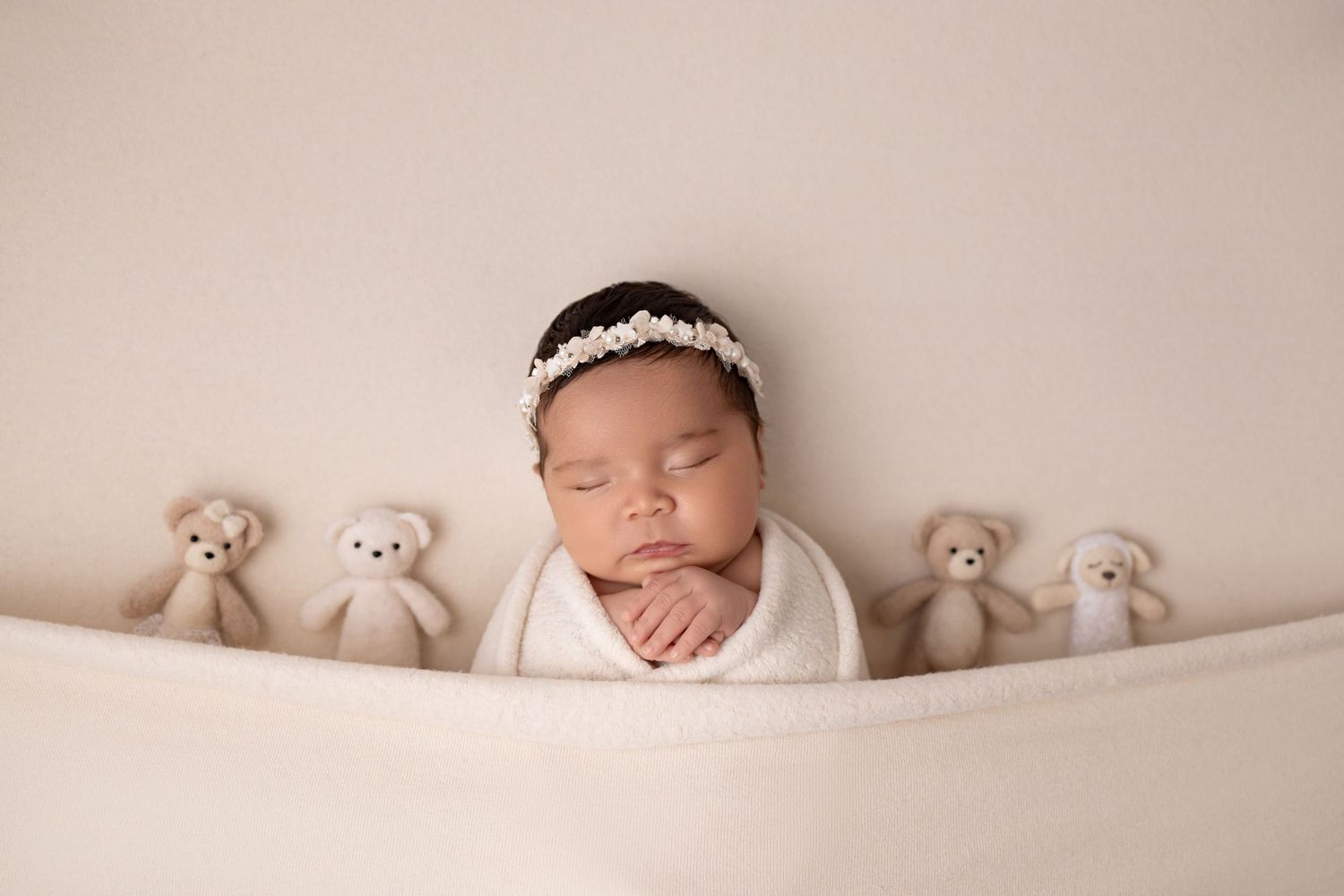 A sleeping newborn swaddled in pink fabric lies on fluffy pink fur surrounded by matching pink roses.