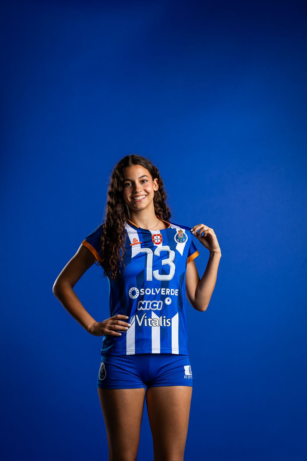Athletic volleyball player wearing blue and white striped jersey number 13 poses against vibrant blue background.