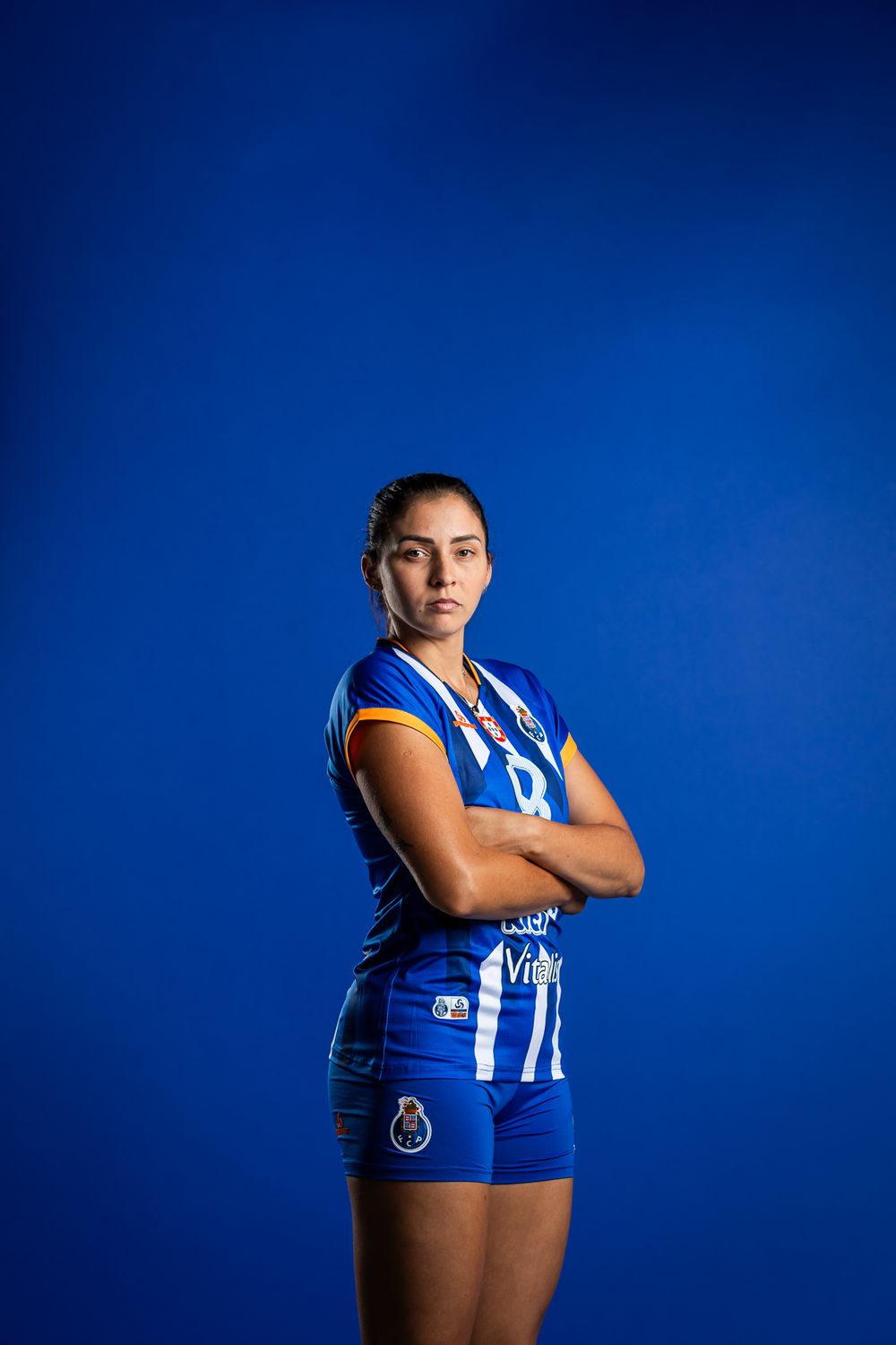 Athletic figure in blue and white FC Porto volleyball uniform stands confidently against blue background.