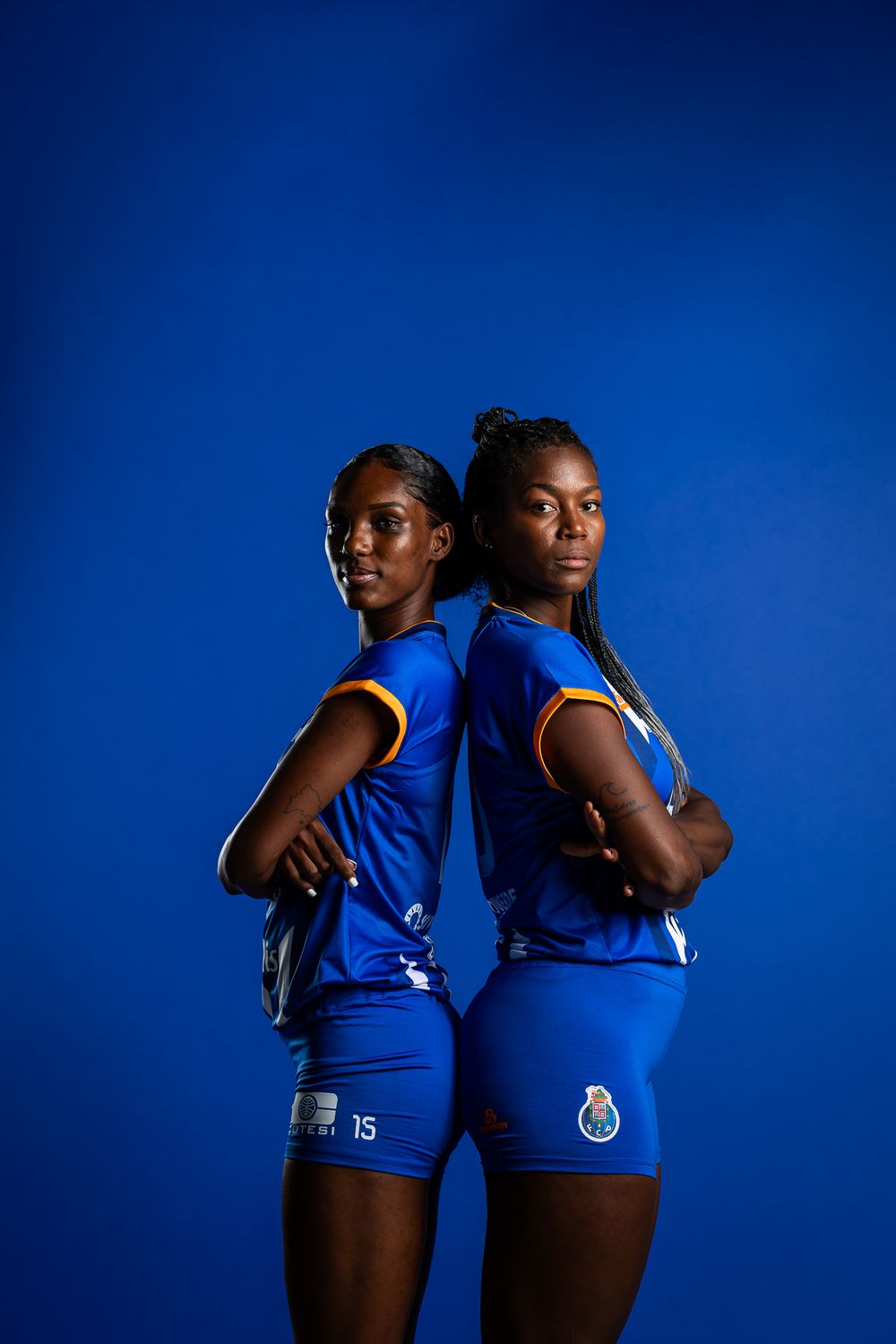 Two athletes pose back-to-back wearing FC Porto blue soccer uniforms against a dark blue background.
