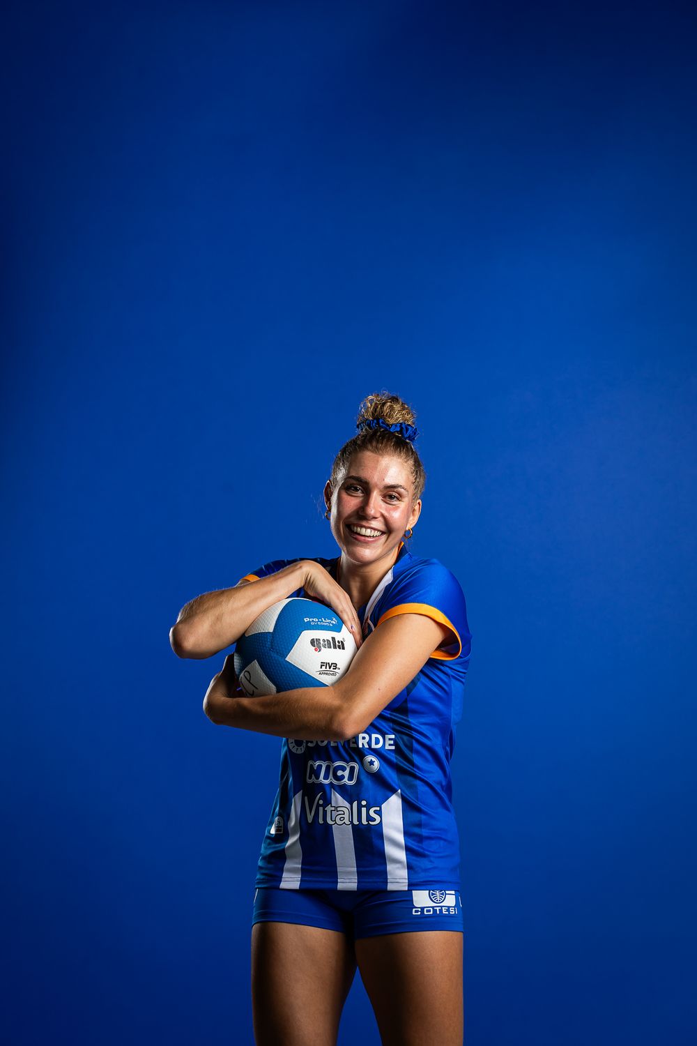 Athlete in blue and white striped uniform holds football against blue background with confident posture.