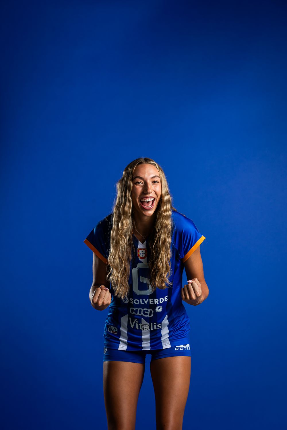 Professional athlete in blue and white uniform shows excitement against vibrant blue studio backdrop.