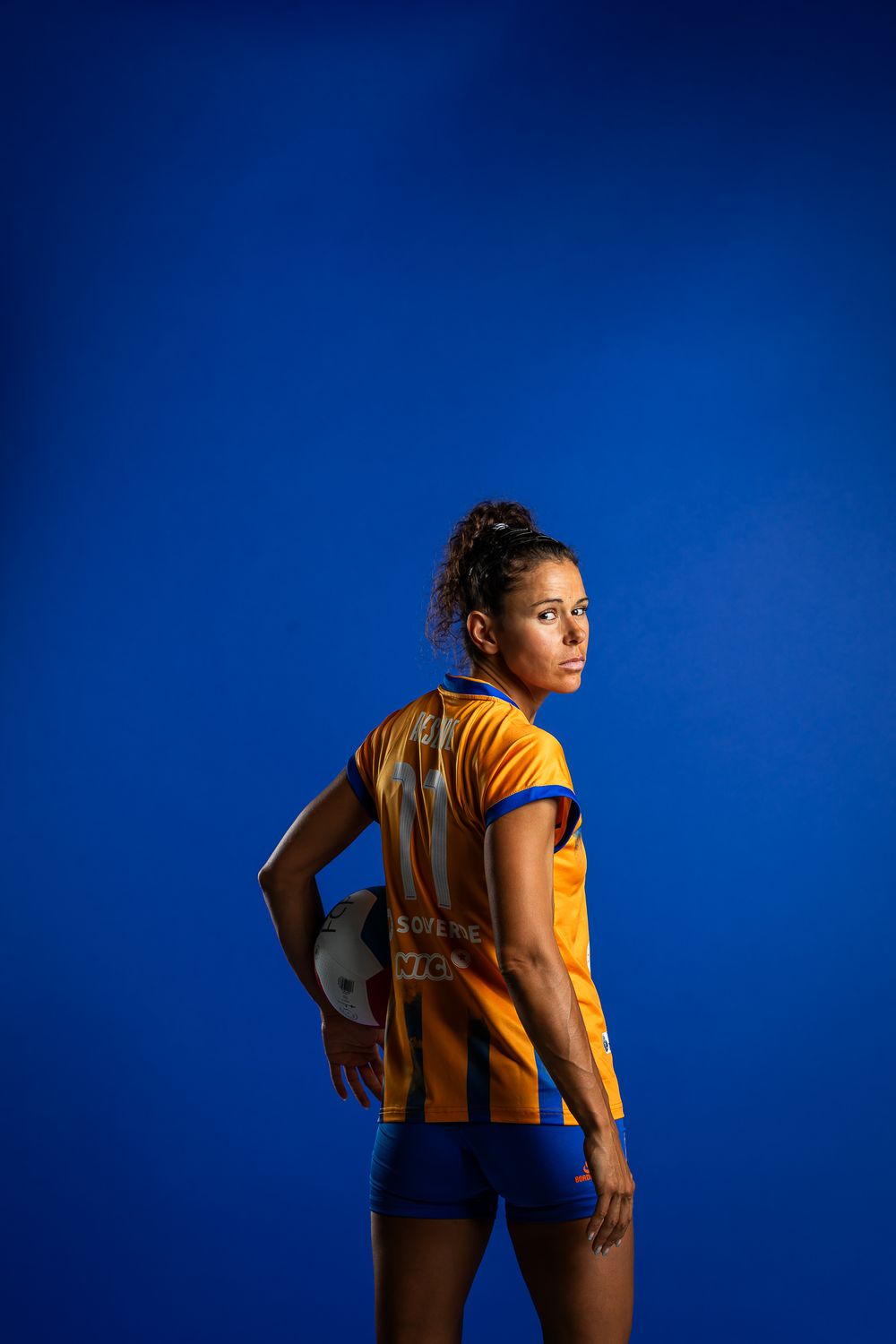 Athletic figure poses in yellow and blue sports uniform against vibrant blue background in studio setting.