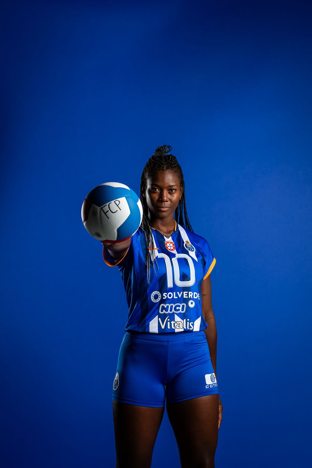Volleyball athlete in blue team uniform holding white ball against vibrant blue background.