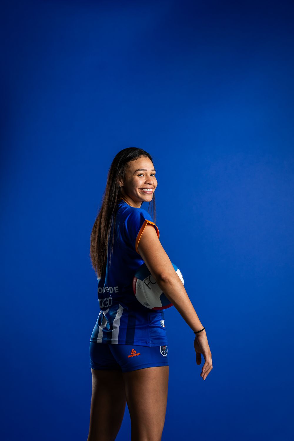 An athlete in a blue uniform strikes a dynamic pose against a vibrant blue backdrop during a sports photo session.
