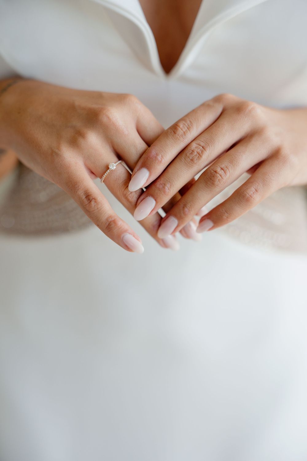 Close-up view of hands with engagement ring against a white background, showing delicate details and sparkle.
