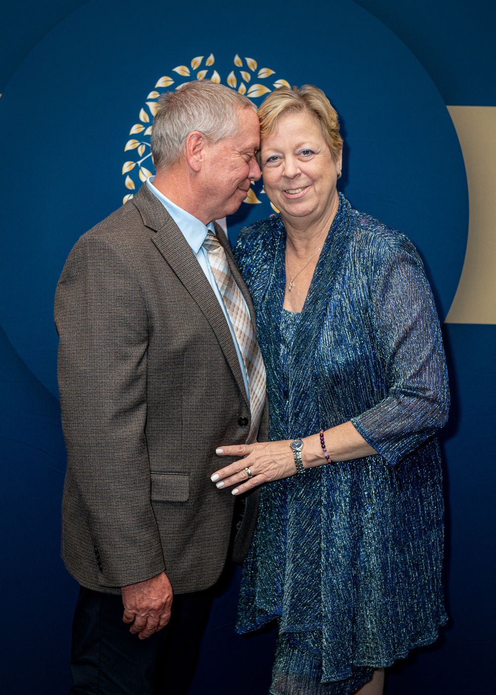 Formal evening event with people in elegant attire interacting against a blue backdrop.