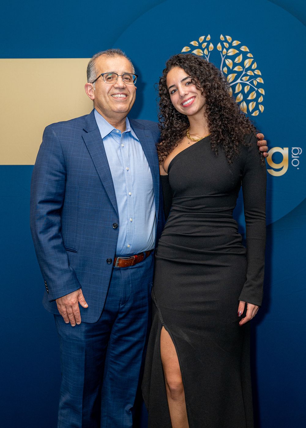 Professional networking event with attendees posing against branded blue backdrop.