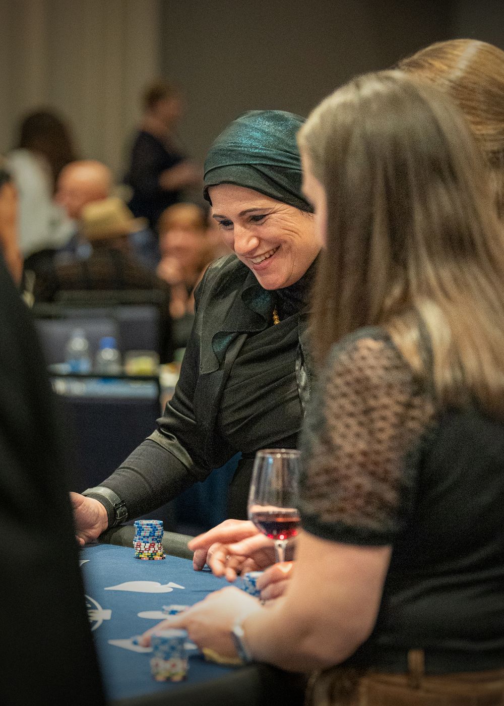 People playing cards at blue-clothed casino tables during a charity gaming event.