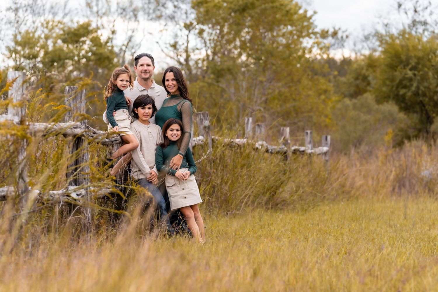 Group enjoying outdoor autumn scenery by rustic wooden fence in tall grass.
