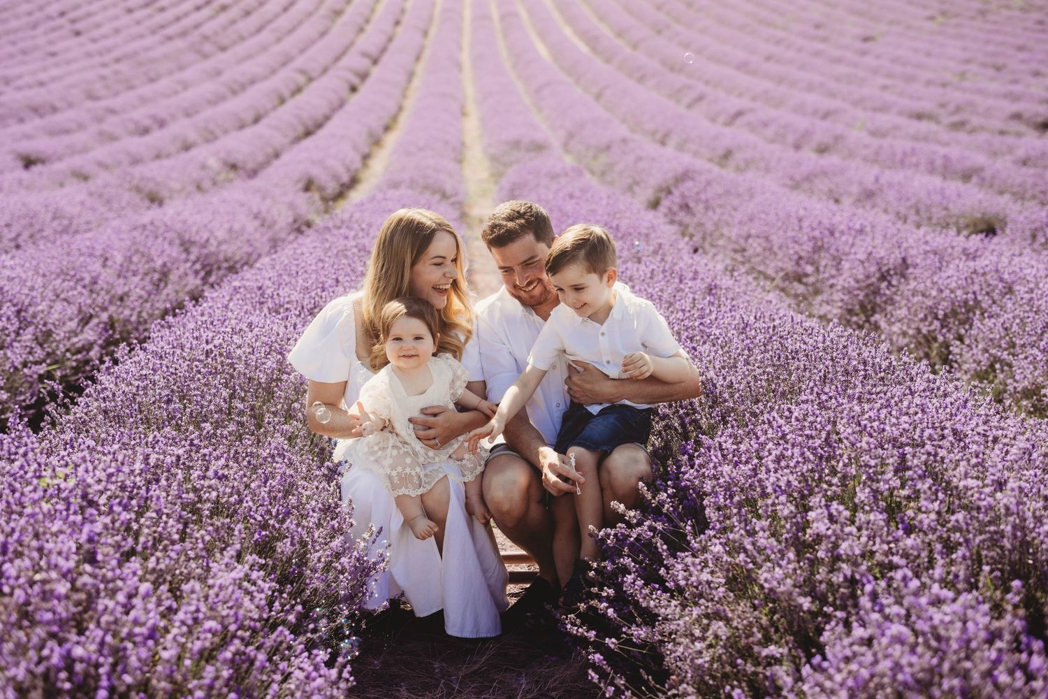 A family sits together in a stunning purple lavender field with rows stretching into the distance during sunset.