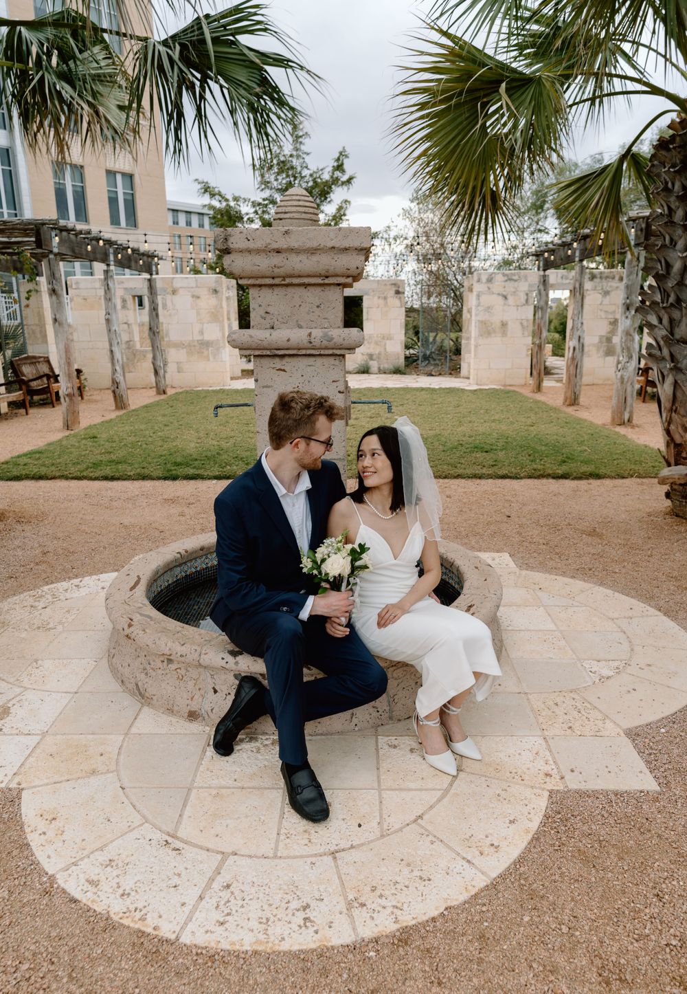 bride and groom sitting on a fountain with palm trees in the background