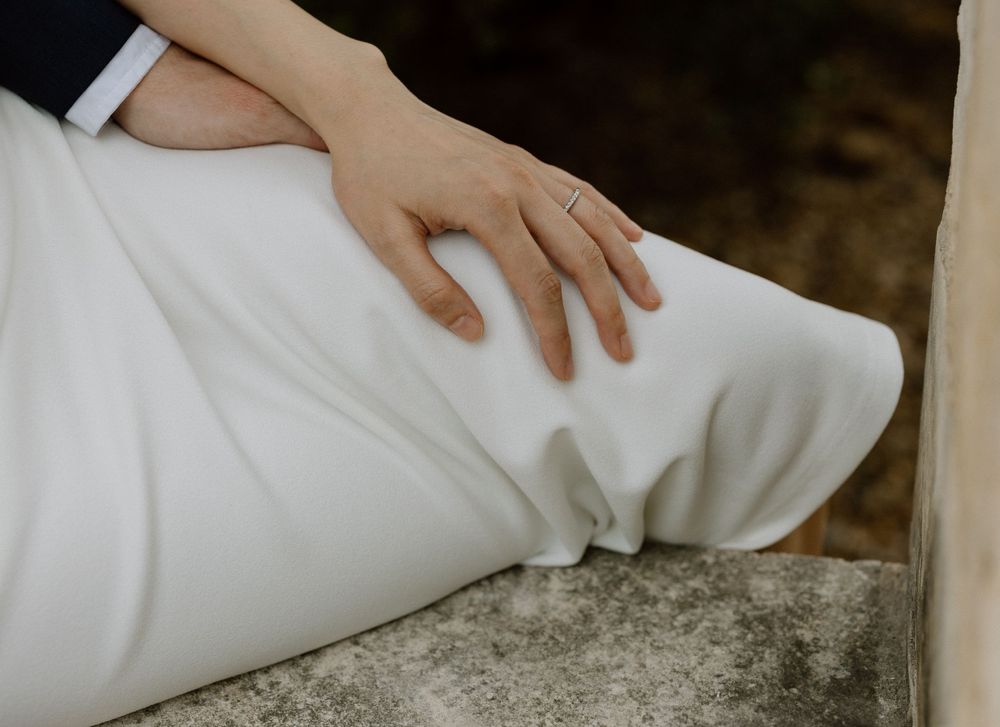 A hand gently rests on flowing white fabric against a textured stone surface in an elegant composition.