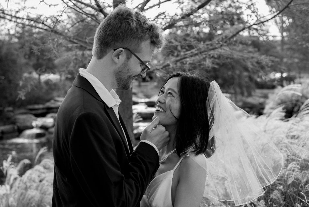 A happy couple shares a joyful moment together in a garden setting captured in black and white photography.