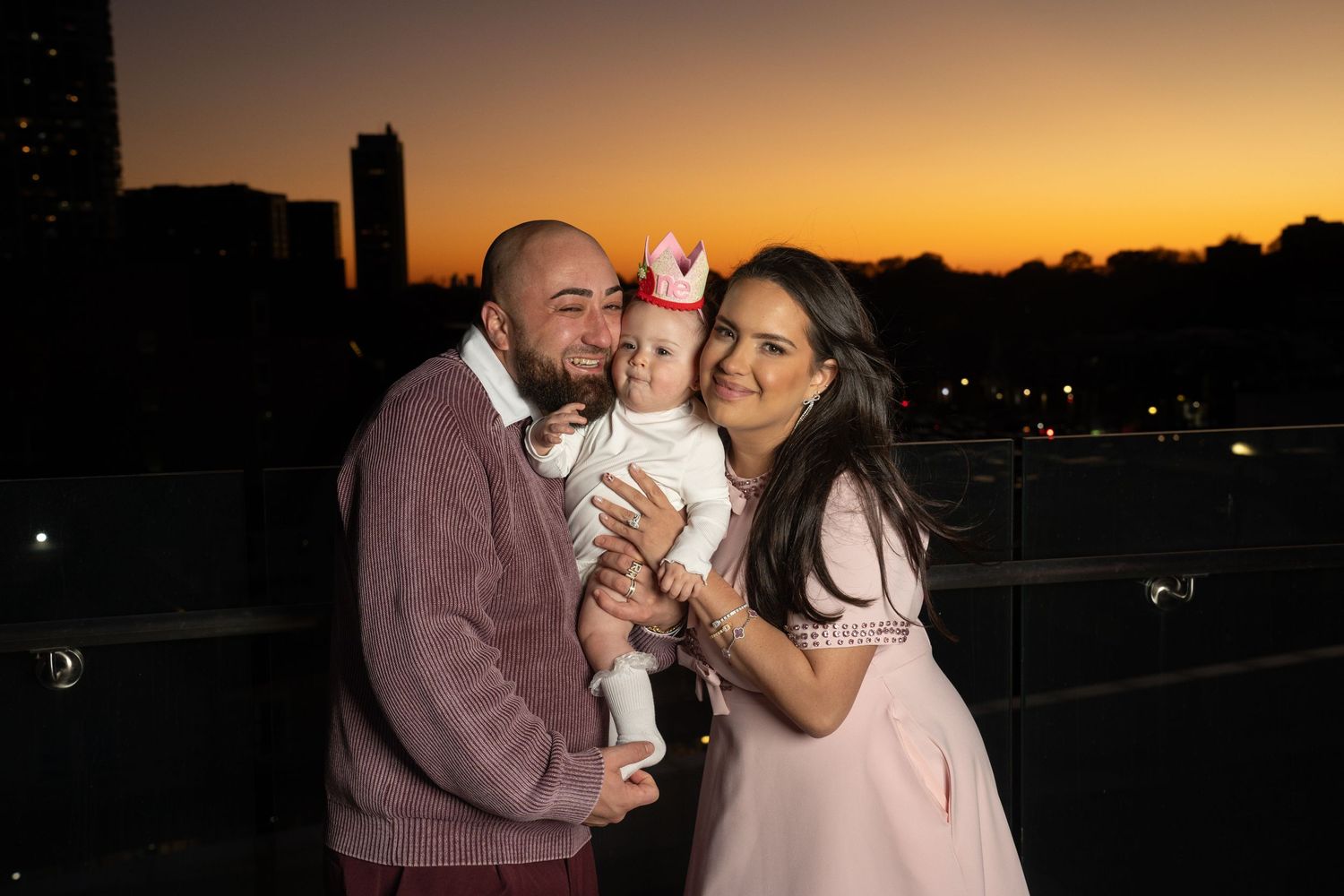 Family embraces during golden sunset photoshoot with warm glowing sky in background.