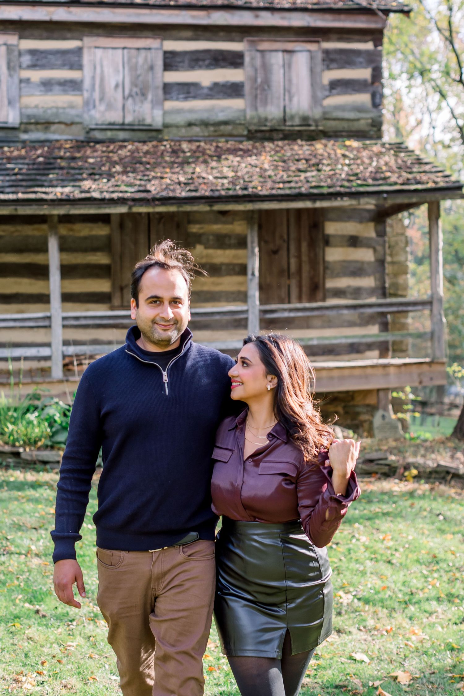 Happy couple posing together outside a historic log cabin structure. Pittsburgh park couple engagement anniversary photoshoot