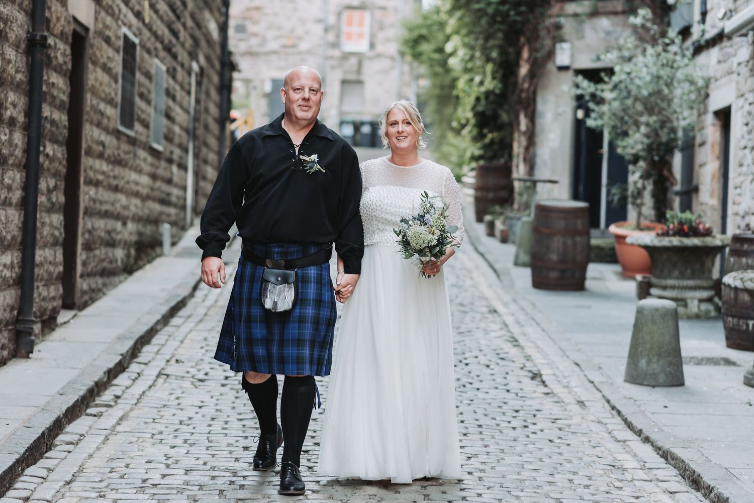 Couple walking down a cobblestone street in Scottish wedding attire.