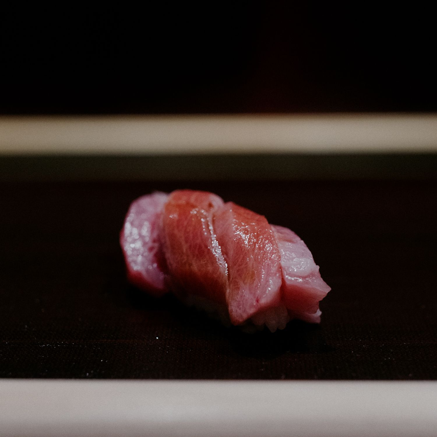 Fresh tuna nigiri sushi with rich red color on dark platter.