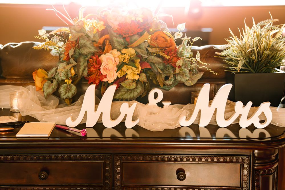 Decorative 'Mr & Mrs' sign with floral arrangement on wooden dresser.