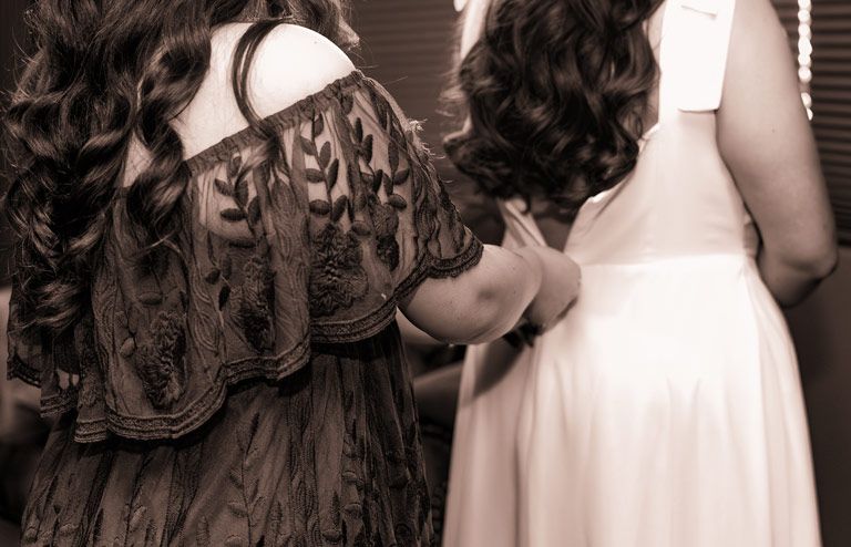 Close up of an intricate lace detail on a teal dress next to a white gown.