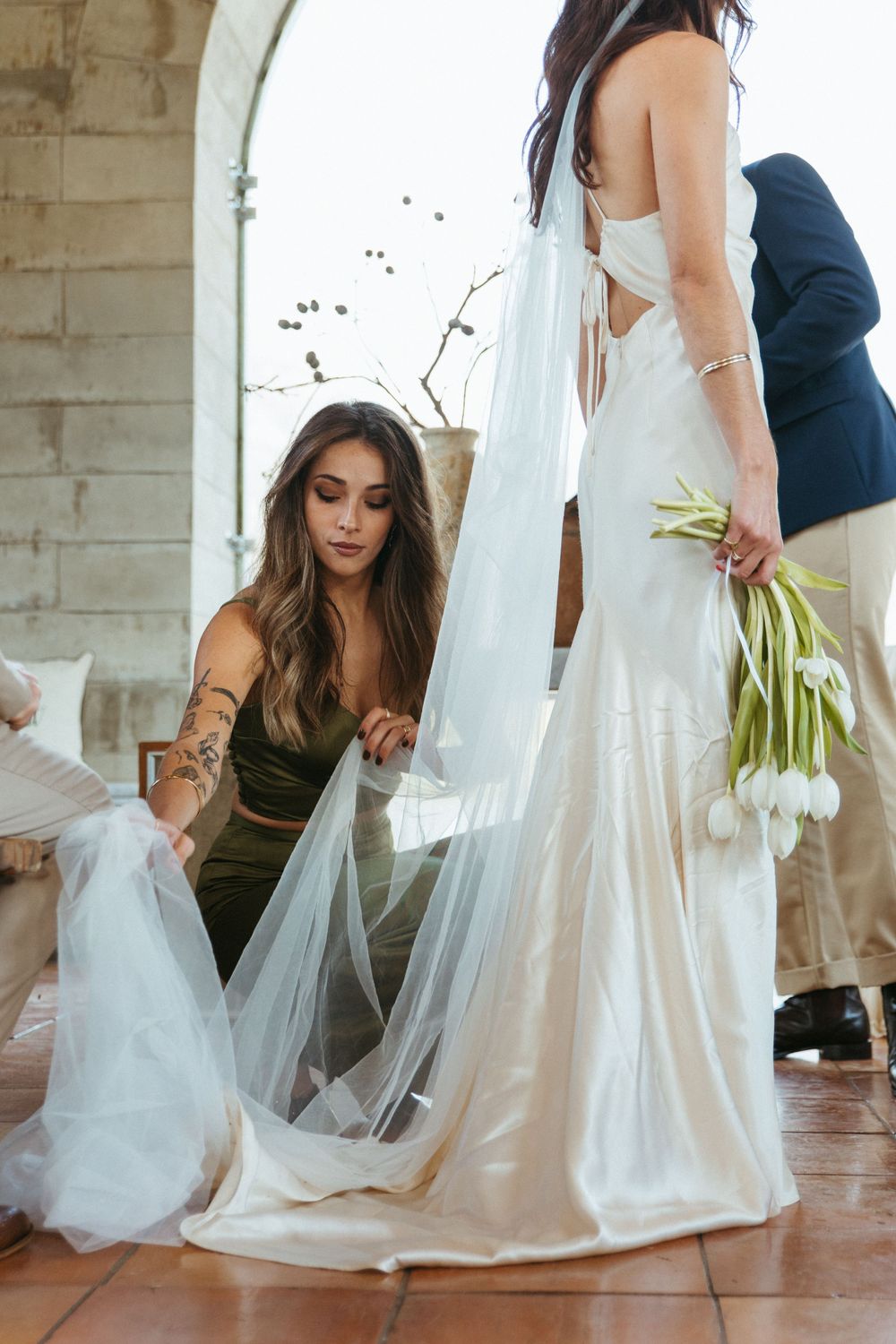 Wedding dress being adjusted during preparation in arched stone venue.