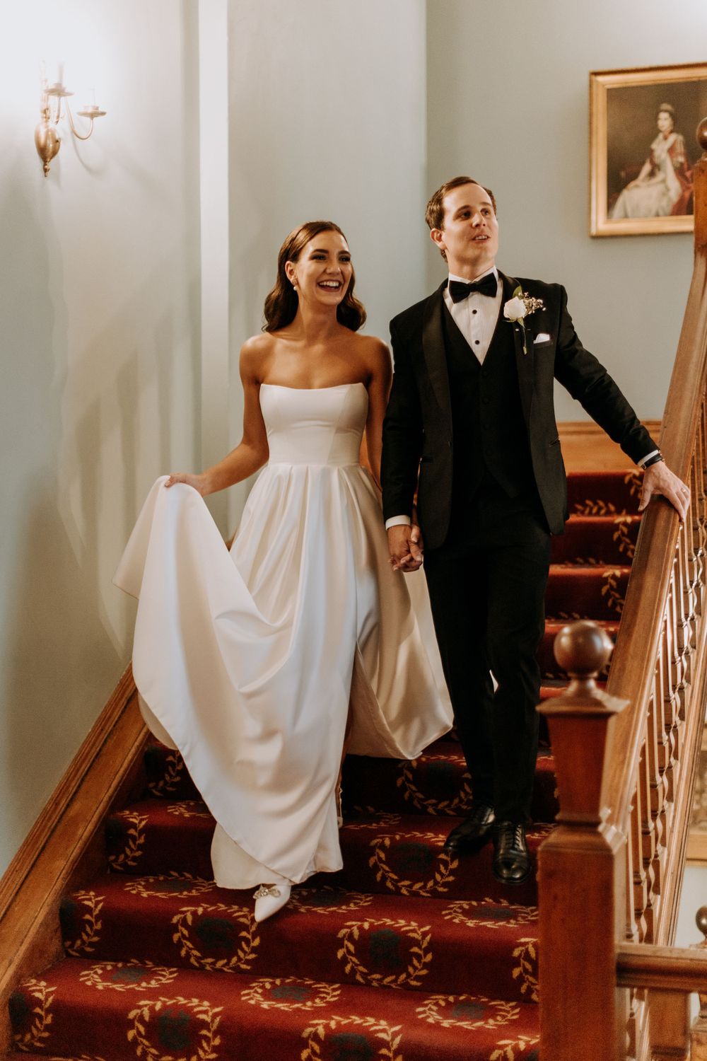 A couple descends an elegant staircase with red carpeting after their wedding ceremony.