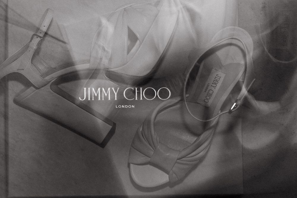 Jimmy Choo London elegant strappy high-heel sandals displayed in a stylish black and white advertisement.