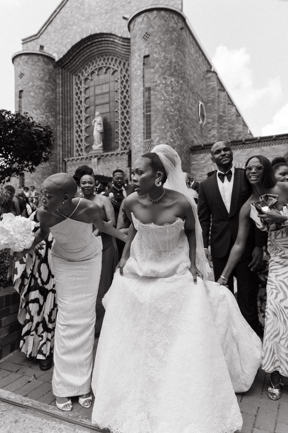 Black and white photo of a bride in a white gown exiting a church surrounded by wedding guests.