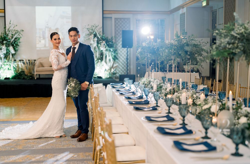 An elegantly decorated wedding reception table with blue and white place settings and floral centerpieces.